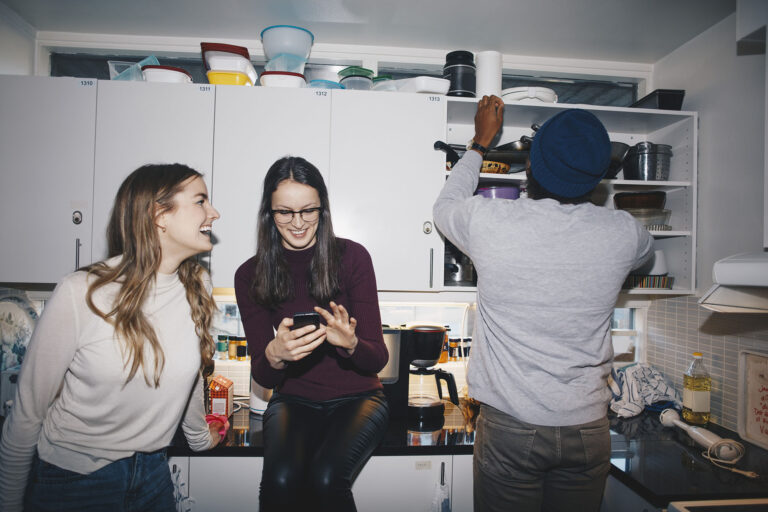 Female friends enjoying by man in kitchen at college dorm