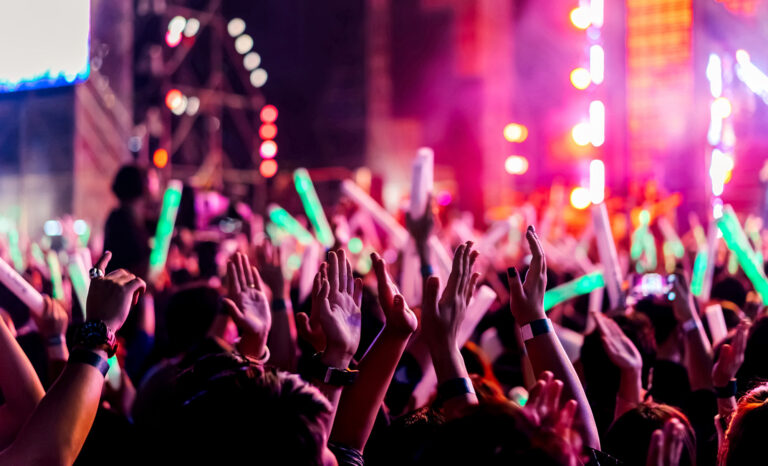Crowd clap or hands up at concert stage lights and people fan audience raising hands silhouette with spotlights glowing effect in the music festival rear view